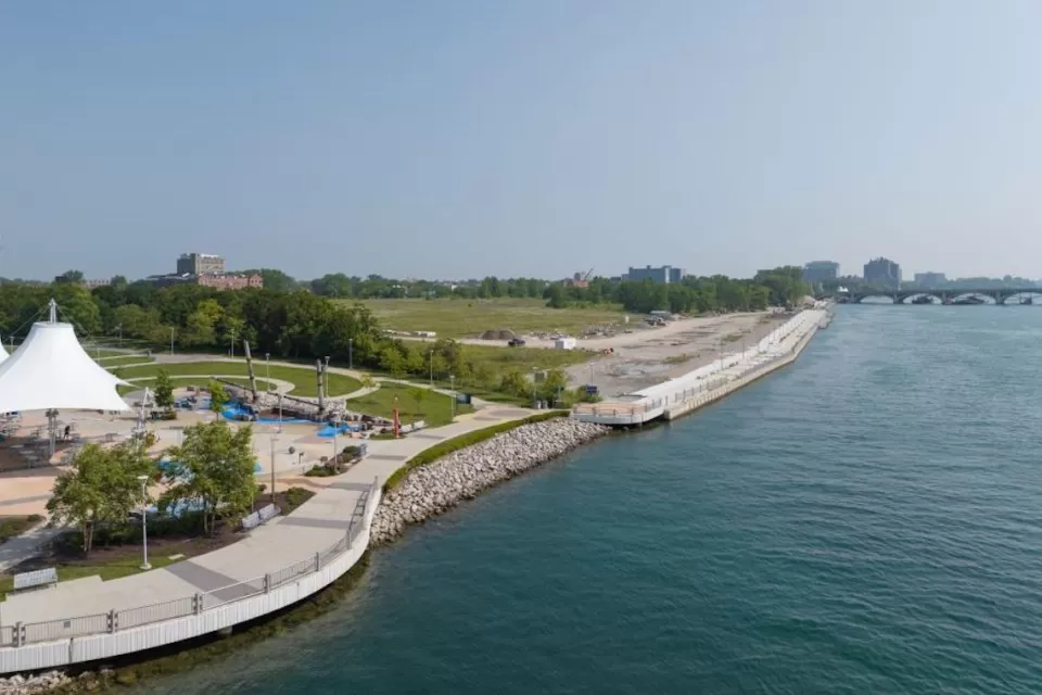 Aerial view of Uniroyal Promenade site on East Riverfront in Detroit with wide paved walkway along river and shaded pavilion at left.